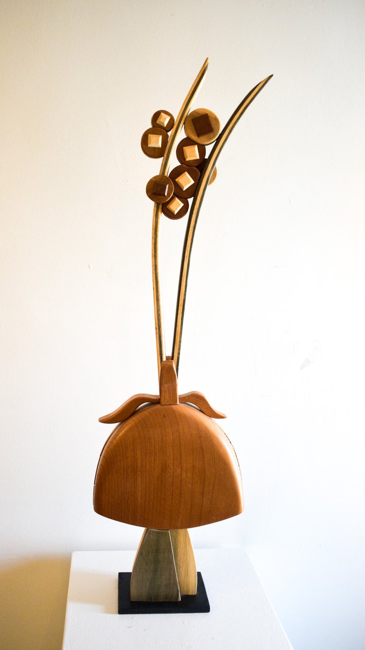 A wooden sculpture with an abstract design, featuring curved wooden elements and a round textured base, displayed against a plain background.