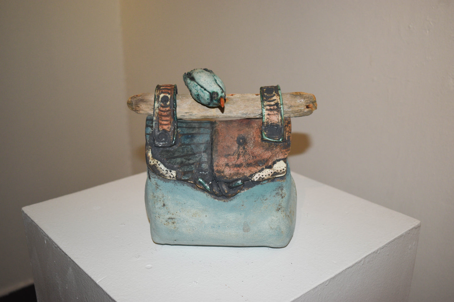 A ceramic sculpture resembling a bag with multi-colored panels and a wooden-like handle with a perched bird