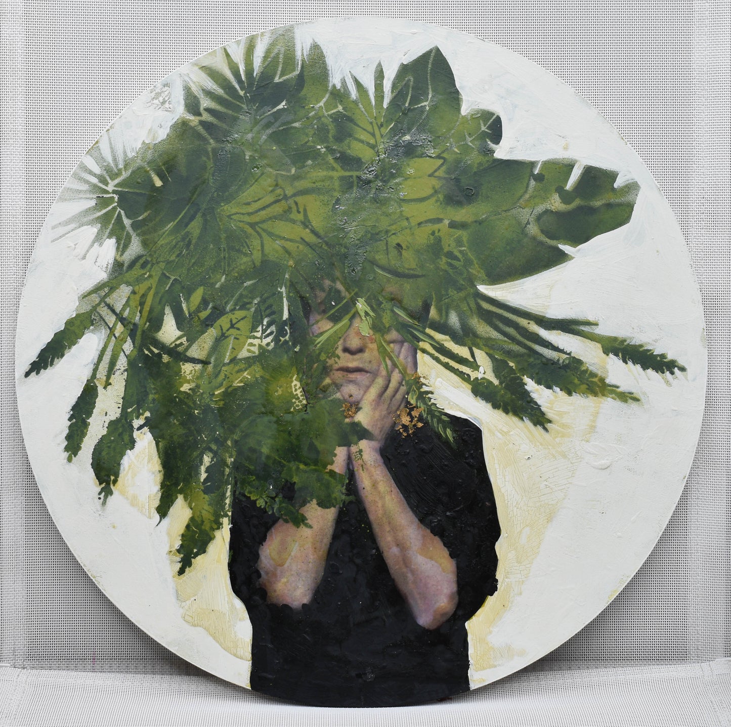 Circular format mixed media artwork of child holding their face with leaves on front
