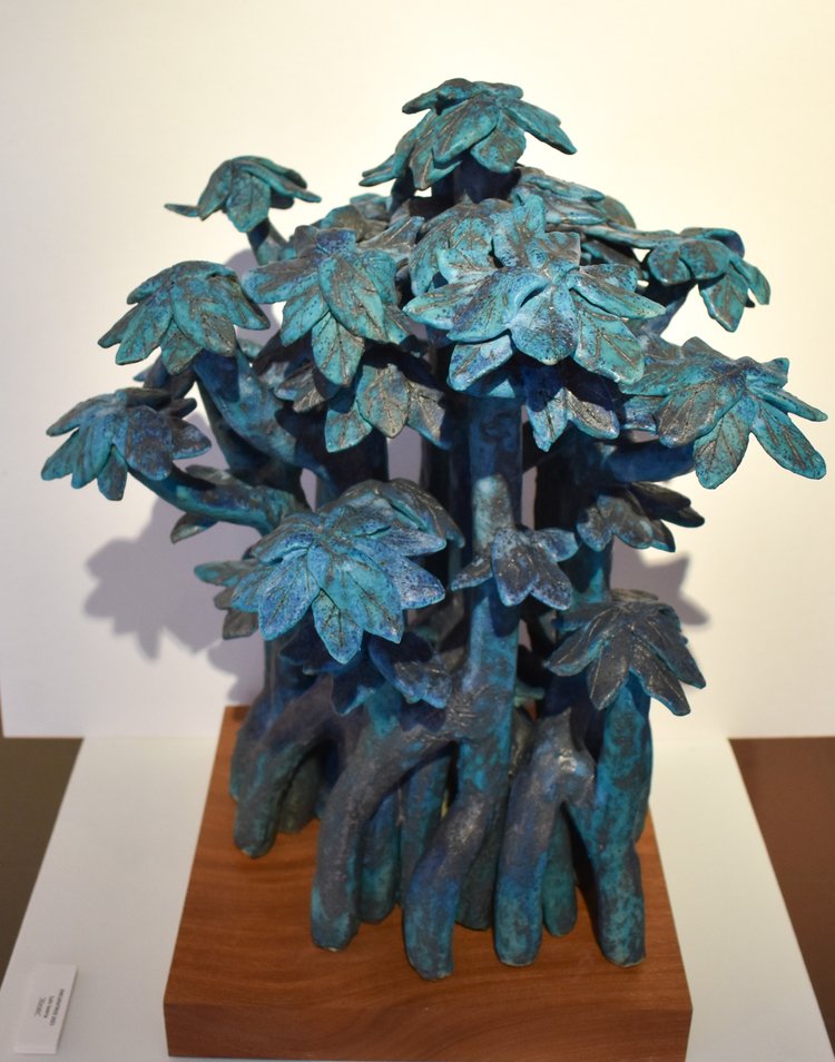 A ceramic sculpture of a tree with multiple branches, displayed on a wooden stand.