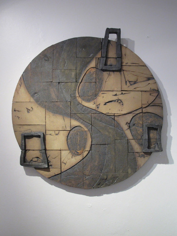 A ceramic mural piece with a geometric pattern, predominantly in brown tones, displayed on a wall.