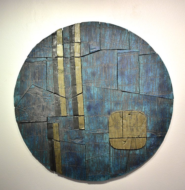 Ceramic mural on wood, with a blue and brown color palette, mounted as a round artwork with a visible join at the center.