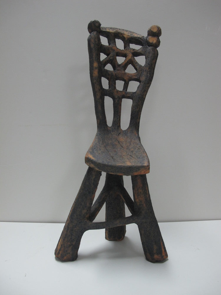 A brown ceramic sculpture of a chair with a geometric pattern on the seat and backrest, exhibiting a rustic appearance.