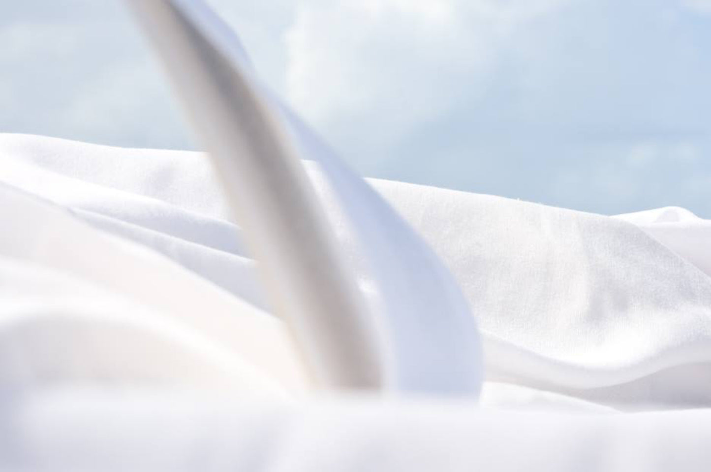 An archival pigment print featuring a white fabric against a soft blue background, giving a sense of motion or ethereality.
