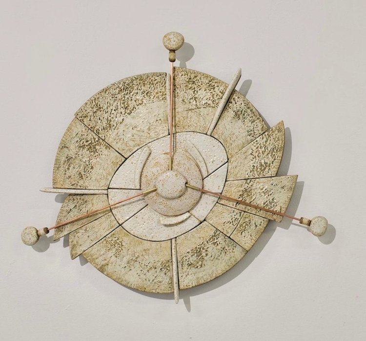 A ceramic mural piece with a geometric design, featuring a central compass-like structure with directional markers and floral details in a beige color palette.