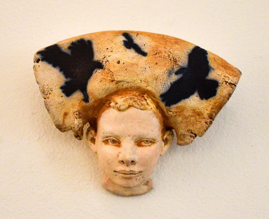 A ceramic sculpture of a stylized female figure with a thoughtful expression, adorned with a black and white piece in a abstract pattern, resembling a headdress.