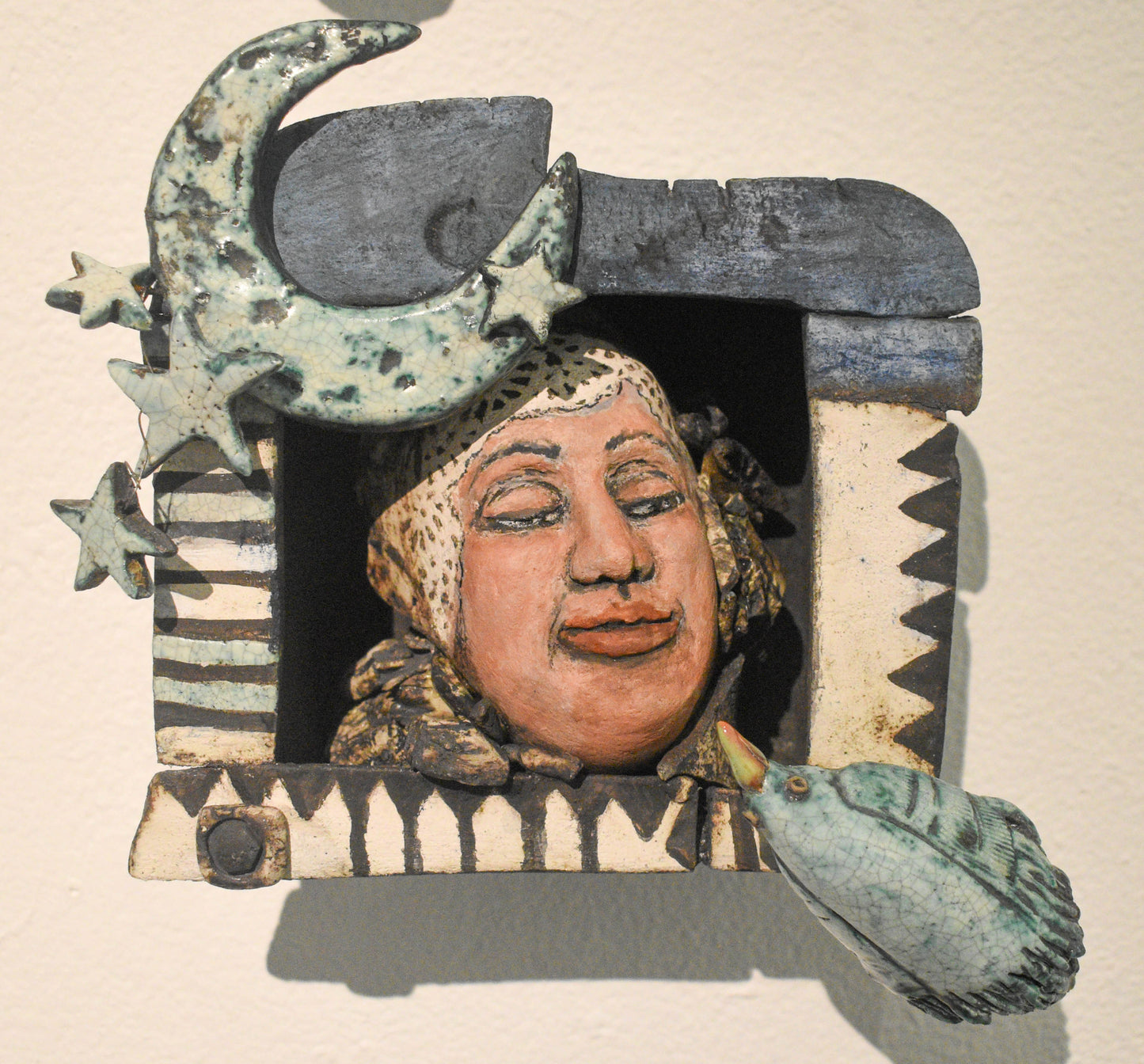 A small ceramic sculpture featuring a whimsical face with stars and geometric patterns.
