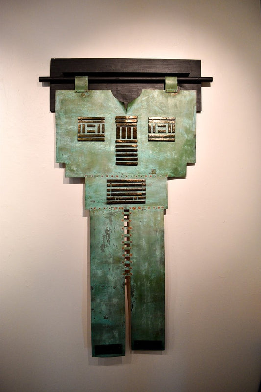 A copper-colored metal sculpture resembling a kimono, displayed on a wall.