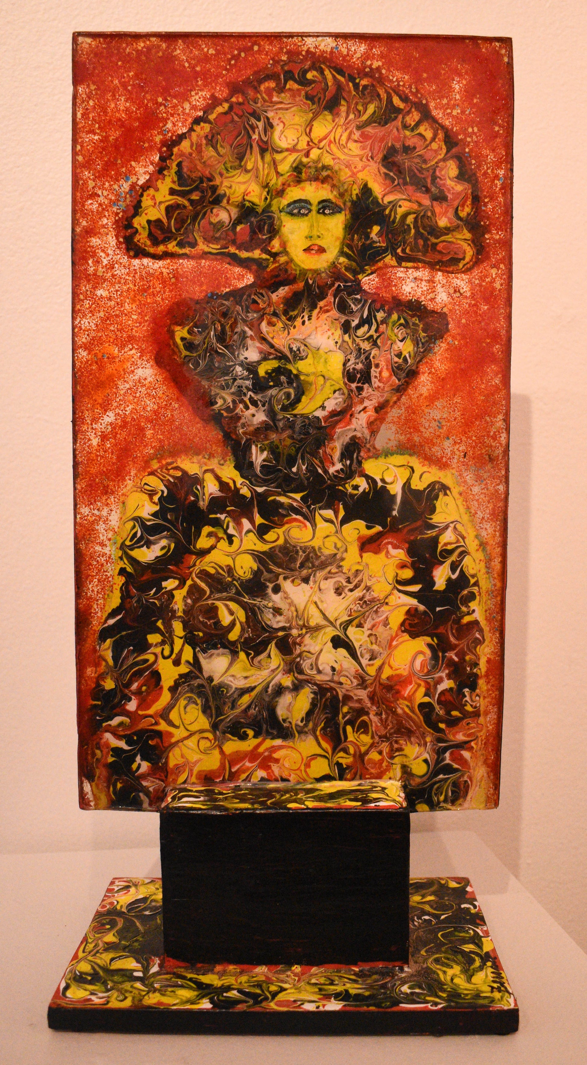 Abstract art piece with central figure of a woman with vibrant fiery colors on a stand.