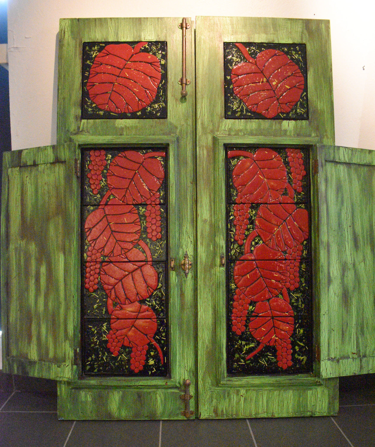 window with a mosaic of red grapes and green leaves on a green wooden background