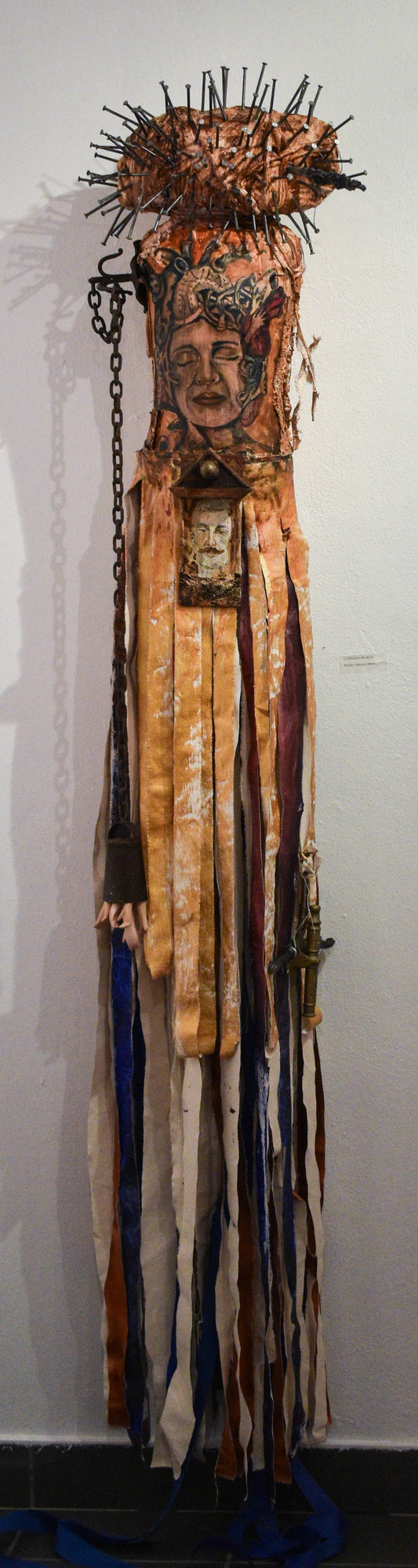 Artistic mixed object sculpture with a painted woman face and a structure full of nails