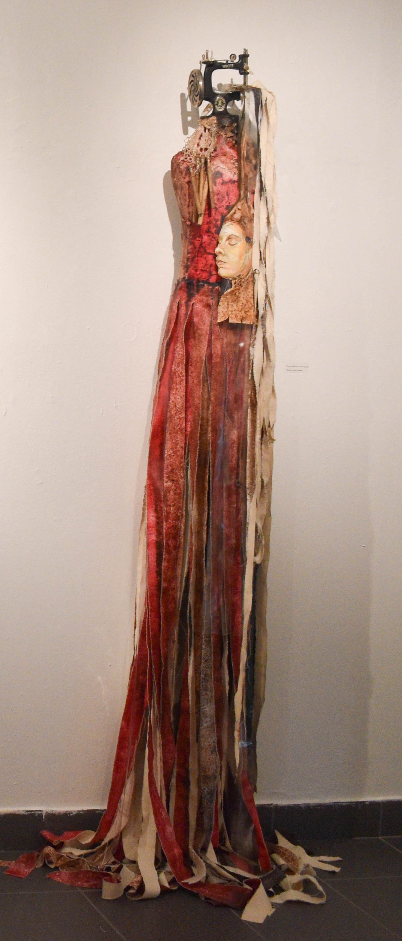 Artistic dress piece made of mixed media with a painted face and attached antique sewing machine
