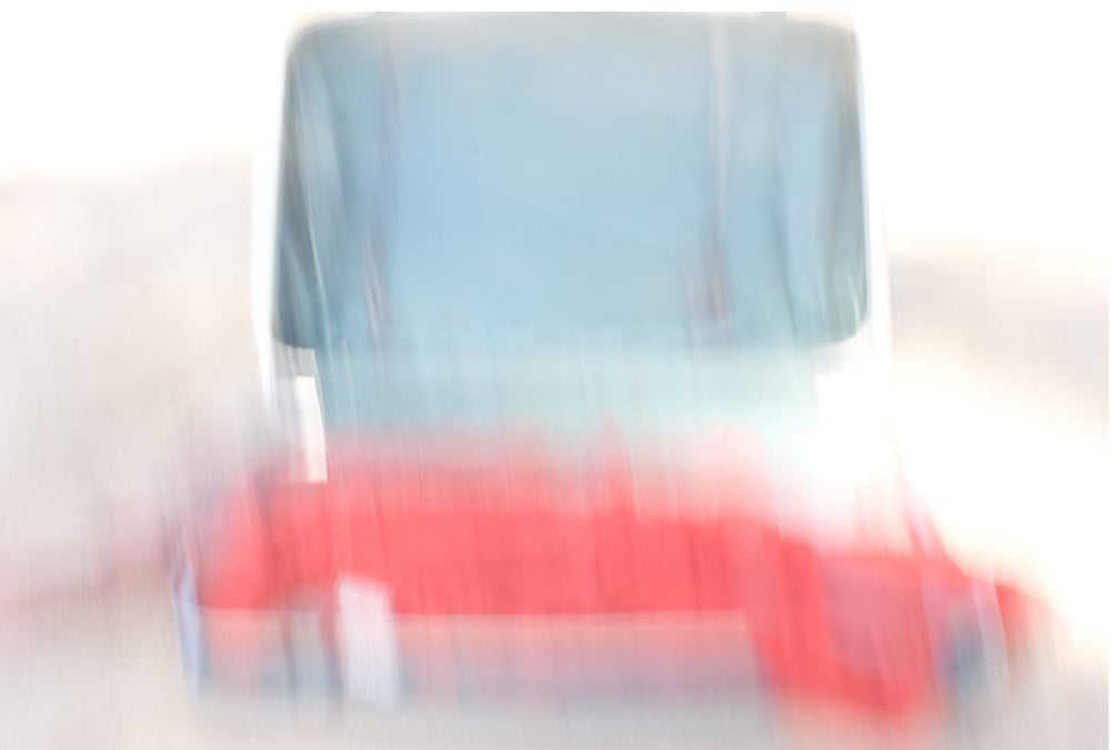 An archival pigment print featuring a blurred image of a red and blue object, possibly a car, with a visible license plate.